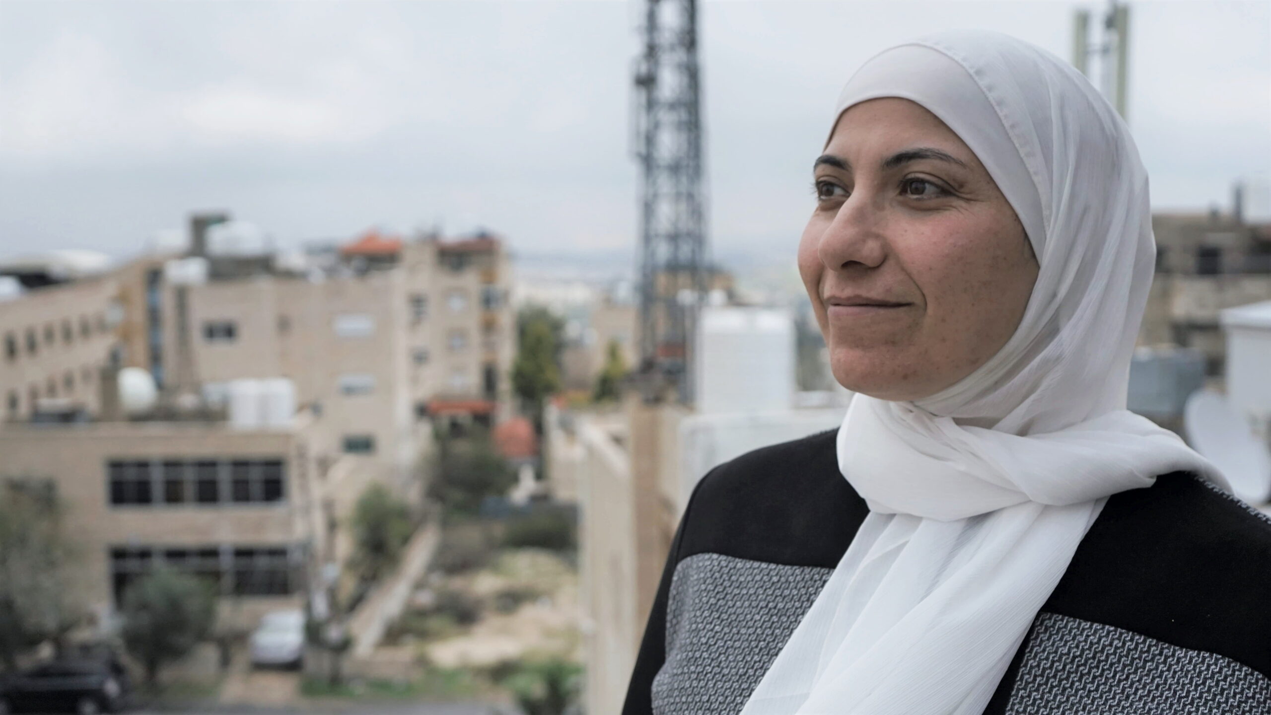 Areej Samreen i fokus foran slørrede bygninger og himmel i jordan